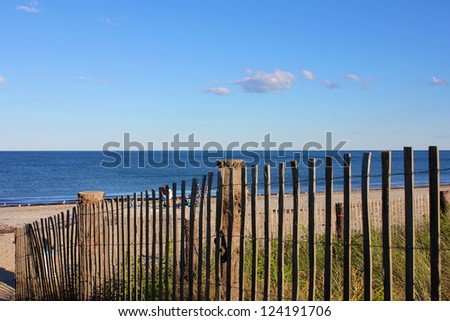 A Cape Cod New England beach lying in the afternoon sun, partly seen through a fence.