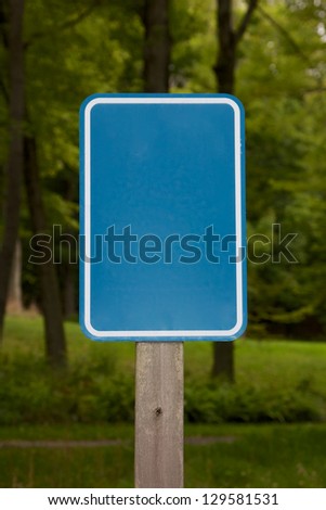 Empty light blue sign before a wooded background. Plenty of copy space.