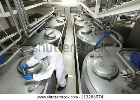 technician in white protective uniform and goggles closing industrial process tank in plant