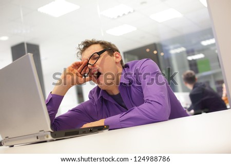 bored yawning businessman working with laptop supporting his head on his hand in office space