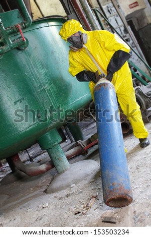 technician in yellow protective uniform, mask, and gloves dealing with steel cylinder with gas