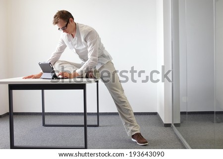 leg exercise during office work - standing man reading at tablet in his office