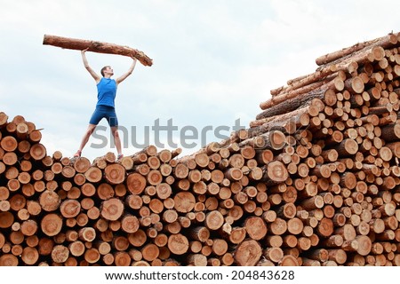 man on top of large pile of logs, lifting heavy log - training