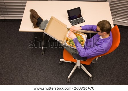 fast meal in office - man sitting at with legs on the desk, heaving break for pizza
