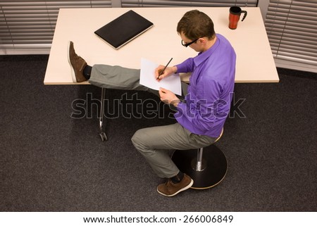 healthy lifestyle at work - business man writing on paper stretching leg,sitting on pneumatic stool in his office