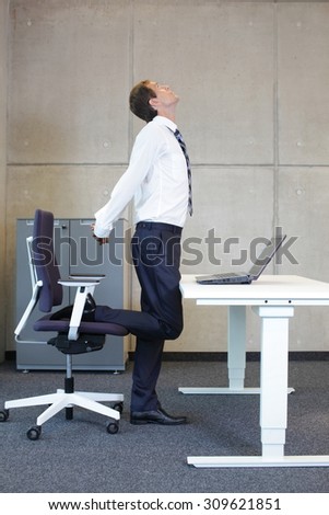 stretching - young businessman in standing position taking short break for exercise in office work