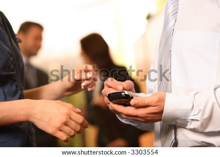 A businessman checks his personal electronic calendar in order to make a new appointment as a co-worker looks on.