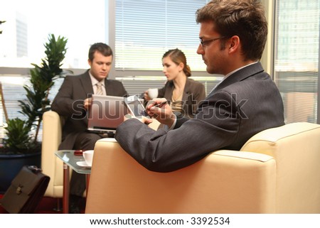 Three young business people siting on leather sofa and working at laptop and palmtop in the office. Two men one woman.