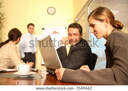 A business team of two men and two women work together with a laptop and a flip chart in a conference room to prepare a new business proposal for a client.