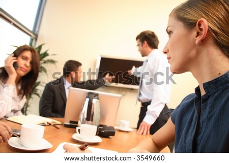 group of four business people at work. one woman is calling on a phone,another is making notes,two men are talking about data at tv screen.