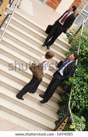 A view of a several people belonging to a business team, standing on the steps of an office building having informal conversation as they leave following an important meeting.