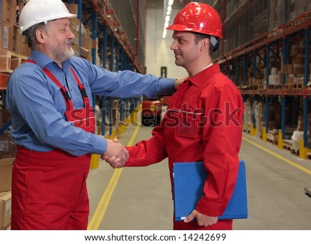 two workers in uniforms warm handshake  in warehouse.one is experienced, young is another