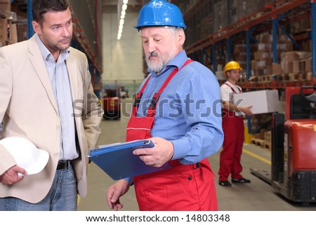 manager and older worker talking over papers in warhouse