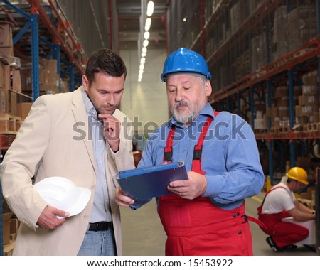 manager and older worker browsing papers in warehouse
