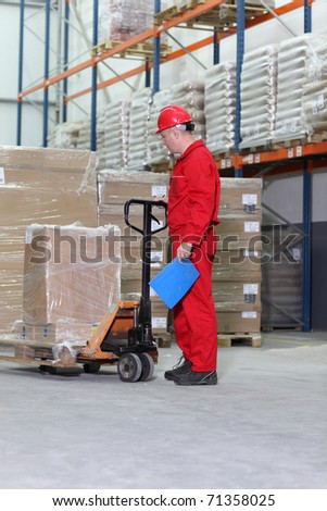 worker in red uniform at work with hand powered pallet jack in warehouse