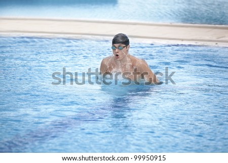Swimmer in cap and goggles taking breath in swimming pool,raising  head  and torso out of the water