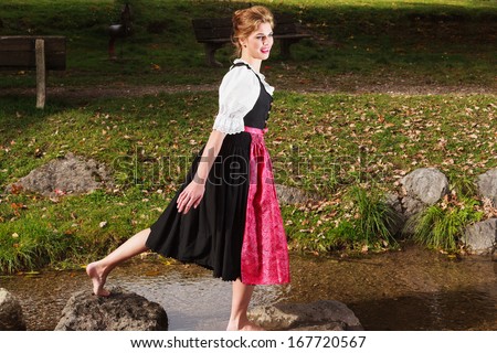 Beautiful barefoot woman playing in a mountain stream in a traditional German dirndl as she enjoys nature /Beautiful barefoot woman in a dirndl
