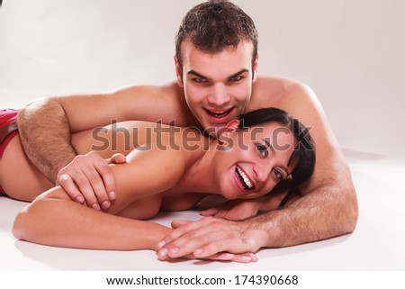 Playful romantic man and woman lying naked on their stomachs in each others arms laughing at the camera / Playful romantic man and woman