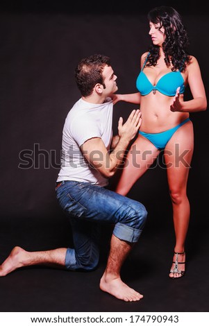 Young couple acting out sexual fantasies of dominance and subservience with the barefoot man kneeling at the woman feet as she stands in her lingerie gripping him by the shirt