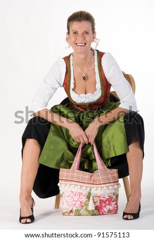 elderly woman in Bavarian costume dress with modern bag is sitting on a chair laughing /elderly woman in Bavarian costume dress with bag