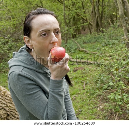 woman biting red apple in woodland