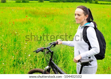 woman resting on bicycle in countryside poppy field