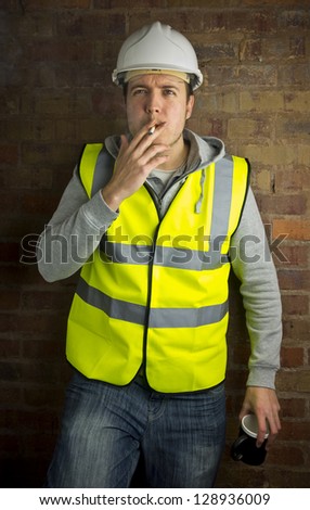 construction worker / builder on coffee / cigarette break leaning against brick wall