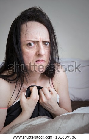 woman covering herself with bed sheets in bedroom looking disgusted