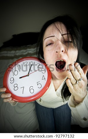 tired woman with clock waking late and yawning sitting on bed