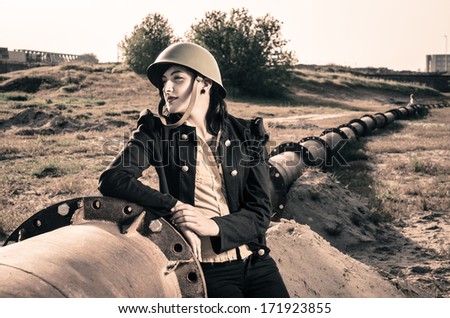 Charming female in army clothes posing next to pipeline.