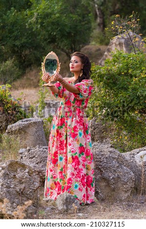 Beautiful woman in bright dress with a mirror on the nature