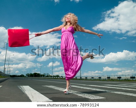 woman in a pink dress with a bag goes over the road
