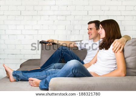Young couple watching TV. Couple on sofa with TV remote.