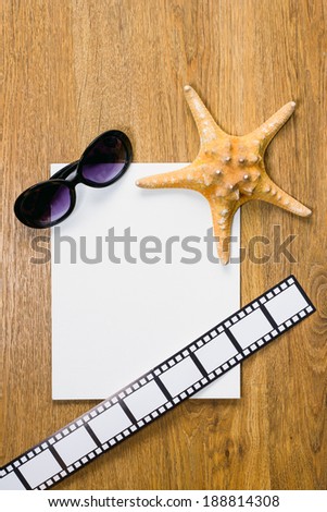 Travel concept collection. Top view of starfish, pair of glasses, film strip and blank white paper on a wooden background.