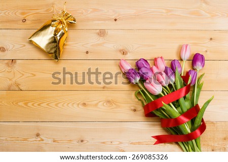 Tulips with red ribbon and gift in gloden bag on natural wooden texture