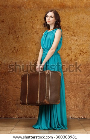 Full length shot of woman in long blue dress holding vintage suitcase