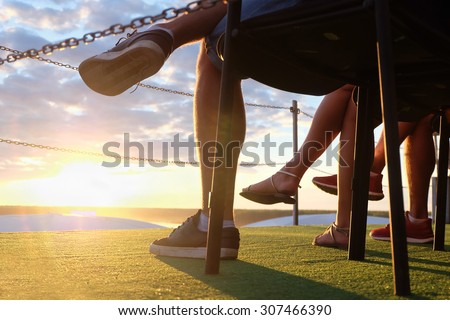 Crossed legs of young people sitting outdoors on sunset. Shallow DOF