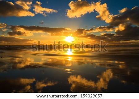Sunset and Clouds Reflection in the Sea at Karekare Beach, New Zealand