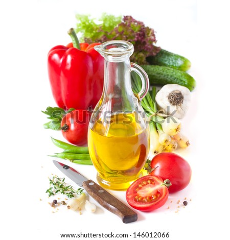 Jug of olive oil and fresh vegetables and spices on a white.