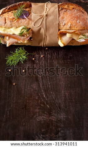 Delicious meat sandwich wrapped in paper with kitchen twine on wood background with copy space for text.