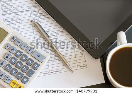 Modern workplace with digital tablet showing charts and diagram on screen, coffee, pen and paper with numbers.