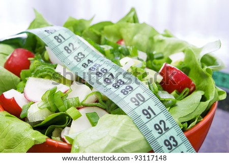 Red bowl with salad on the table in the kitchen with meter to measure waist