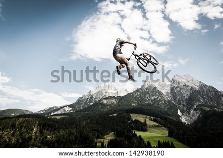 biker jumps a high stunt with mountains in the back