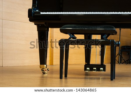 part of grand piano with music stool at wooden floor