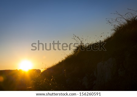 sun while sunset behind rock on mountain with grass silhouette