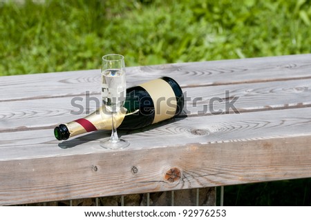 empty sparkling wine bottle with glass lying on a wooden bench