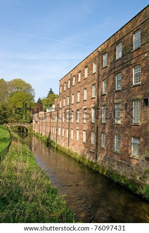 Cotton mill dating from the industrial revolution beside a river which once powered a waterwheel in the mill against a blue sky