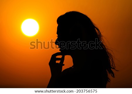 Silhouette of a woman touching her chin with her hand at sunset.