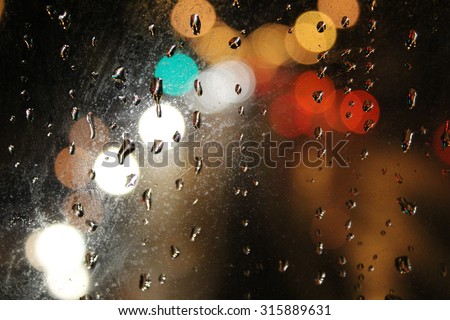 Night city through wet window. Raindrops on the glass, on a background of the night city.