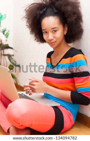Black African American student teenage girl with a afro haircut seated on the floor using a laptop computer